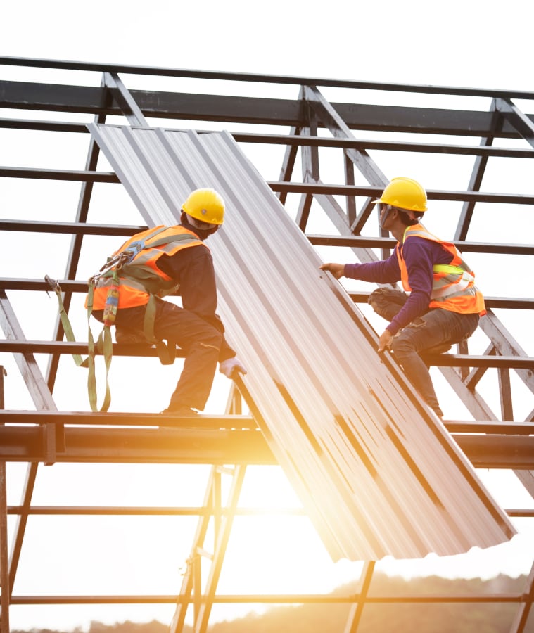 Roofers in hard hats and safety vests installing metal roofing panels