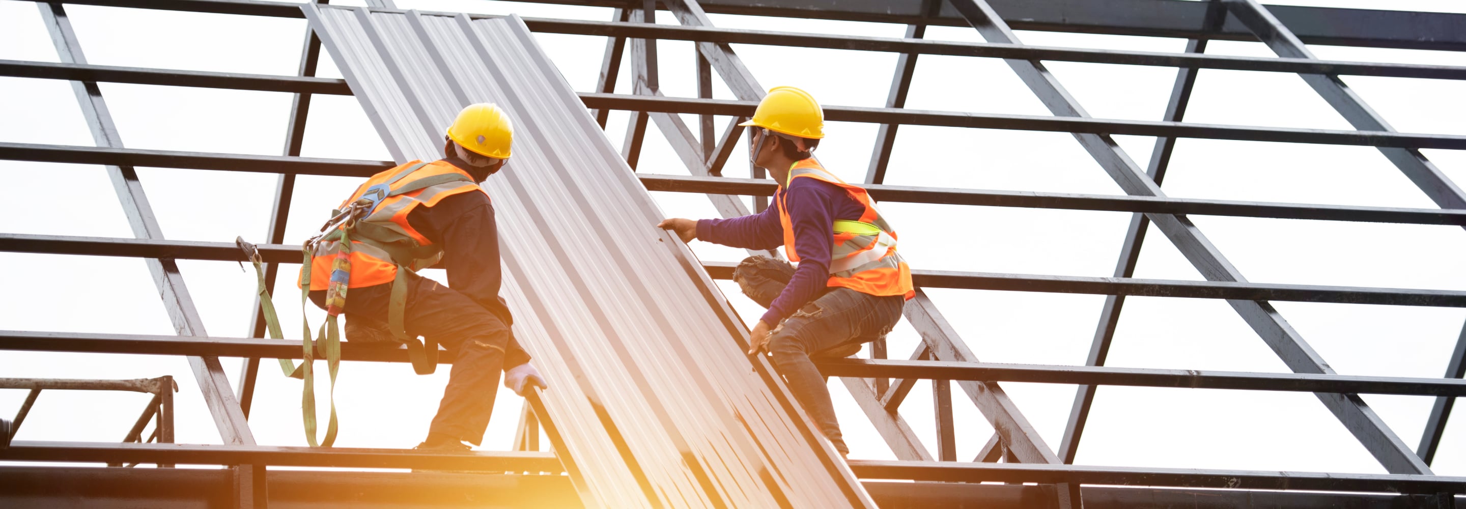 Roofers in hard hats and safety vests installing metal roofing panels