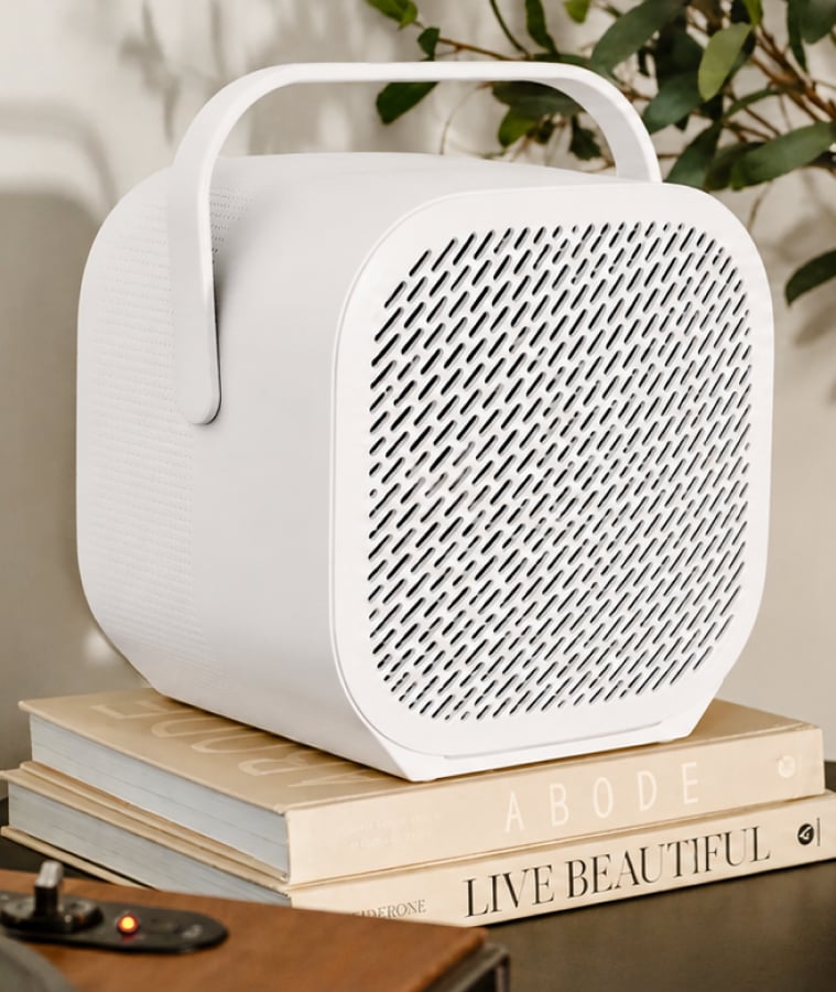 White portable air purifier on a stack of books beside a potted plant