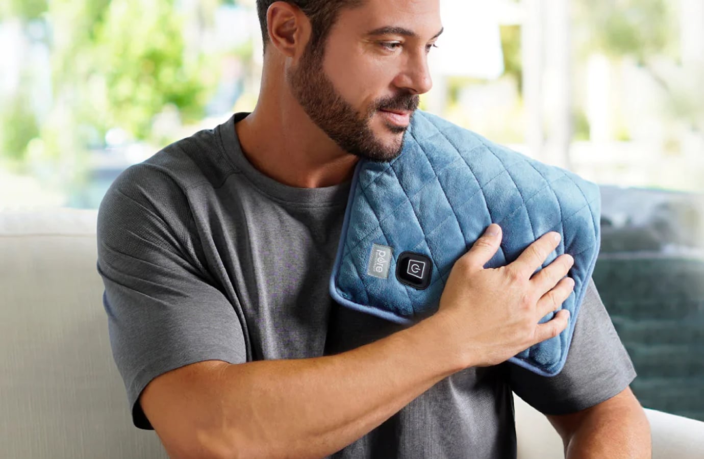 Man using a blue heated wrap on his shoulder at home, representing Bear Down Brands wellness products