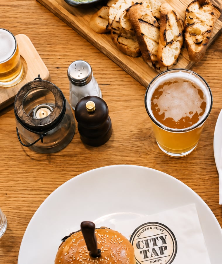 Craft beer and a burger served on a wooden table at a City Tap House restaurant