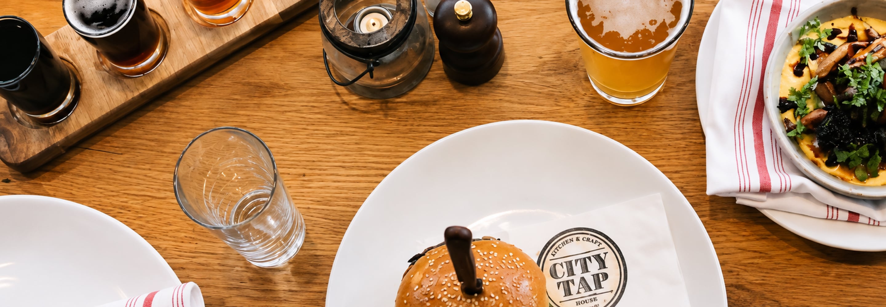 Craft beer and a burger served on a wooden table at a City Tap House restaurant