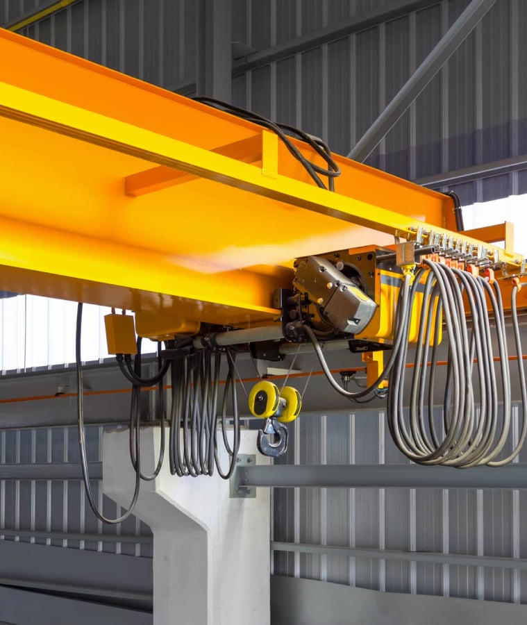 Yellow overhead crane hoist and cables inside an industrial facility
