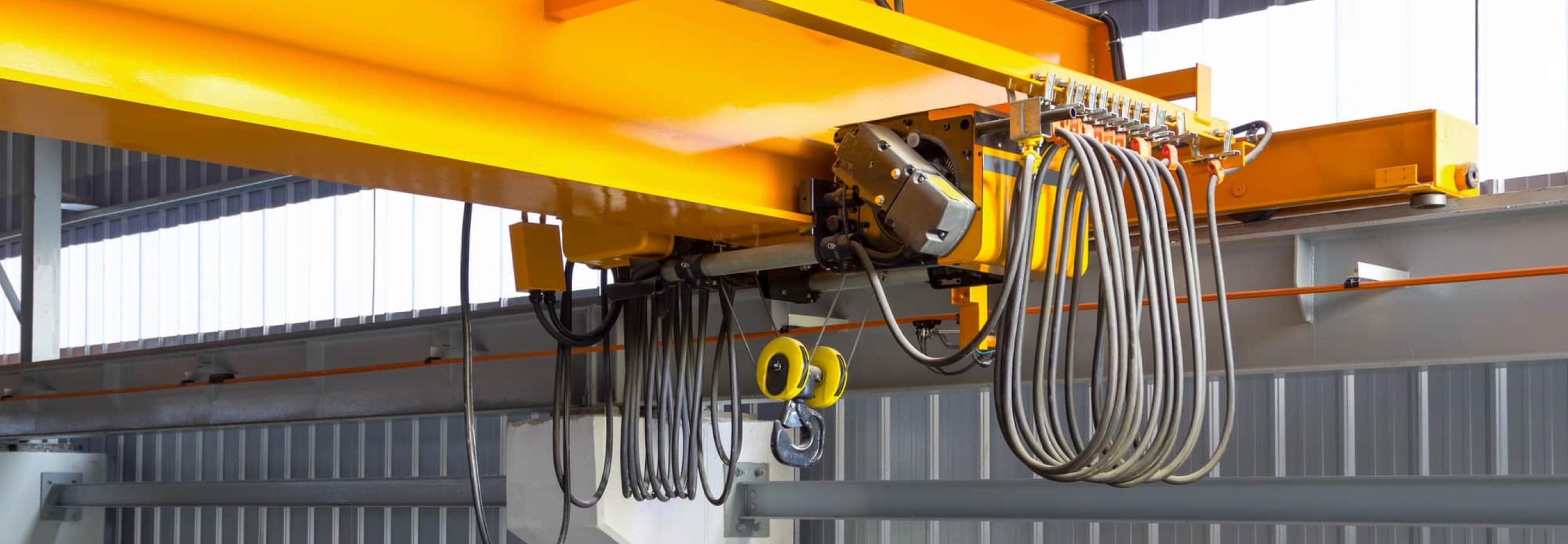 Yellow overhead crane hoist and cables inside an industrial facility