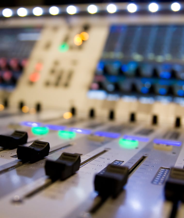 Close-up of a radio station broadcast mixing console with illuminated faders