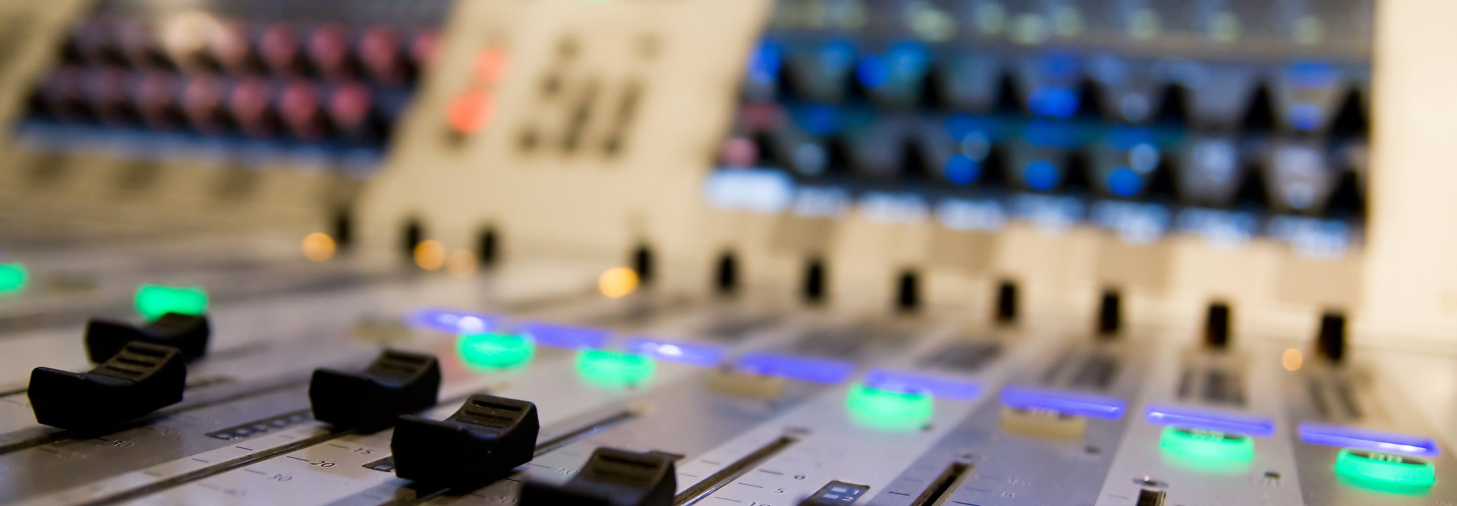 Close-up of a radio station broadcast mixing console with illuminated faders