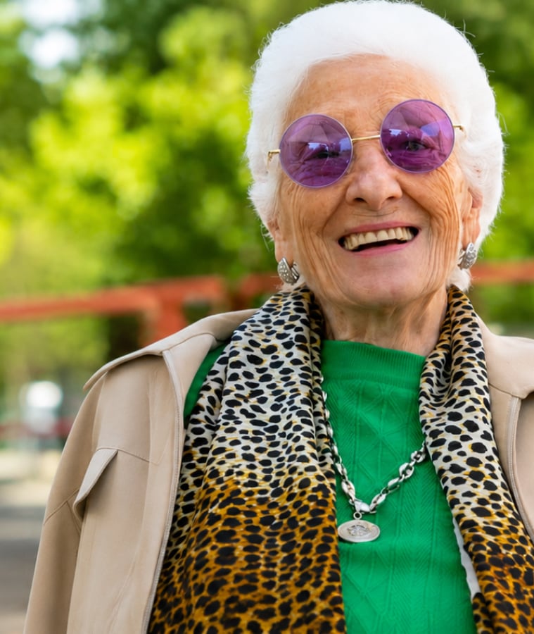 Smiling elderly woman with white hair and purple glasses outdoors