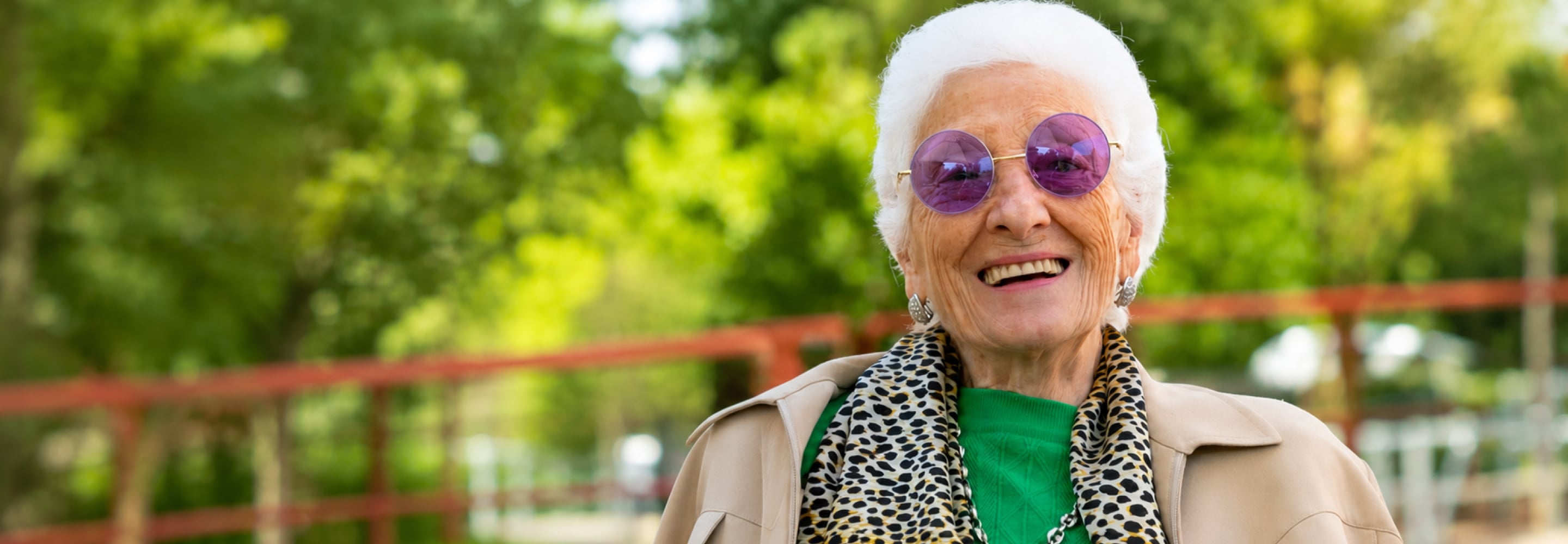 Smiling elderly woman with white hair and purple glasses outdoors