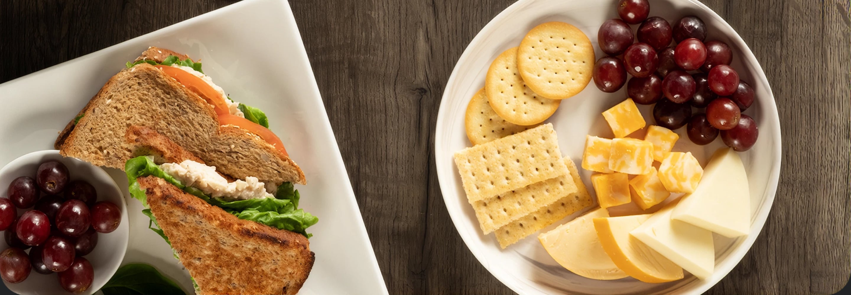 Prepared sandwich next to a snack plate of crackers, cheese, and grapes