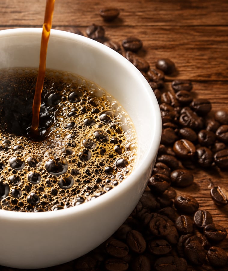 Fresh coffee pouring into a white cup surrounded by roasted coffee beans