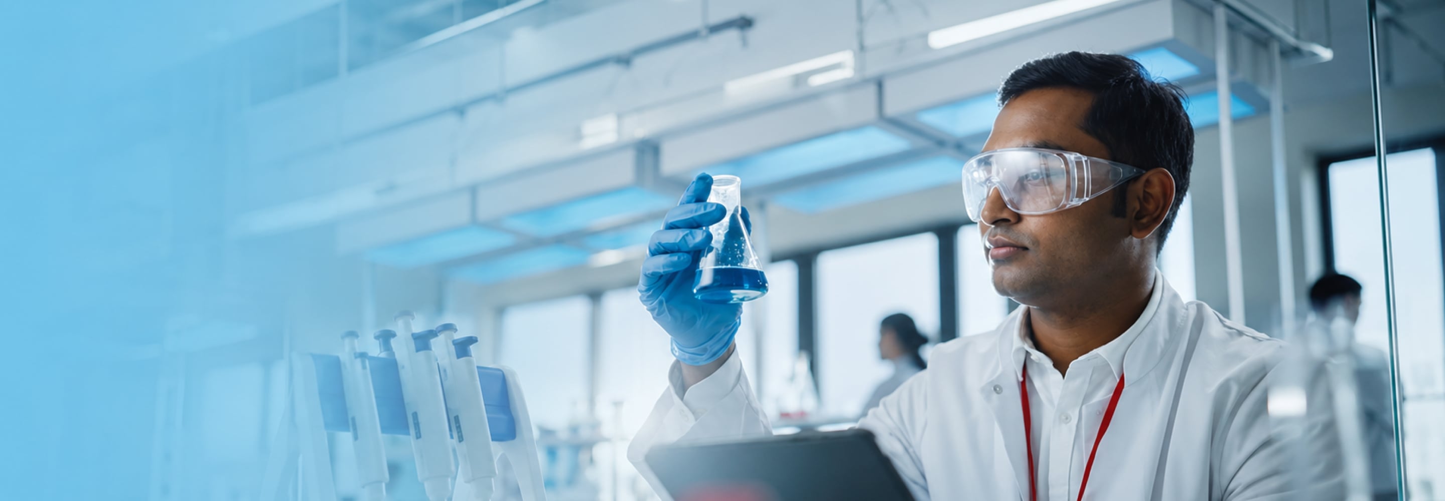 Lab scientist in safety glasses examining a sample vial in a laboratory