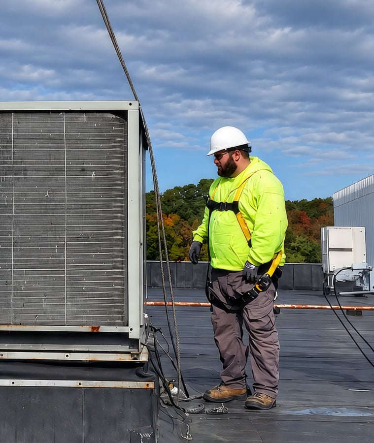 HVAC technicians in hard hats guiding a commercial rooftop unit as it is lifted into place
