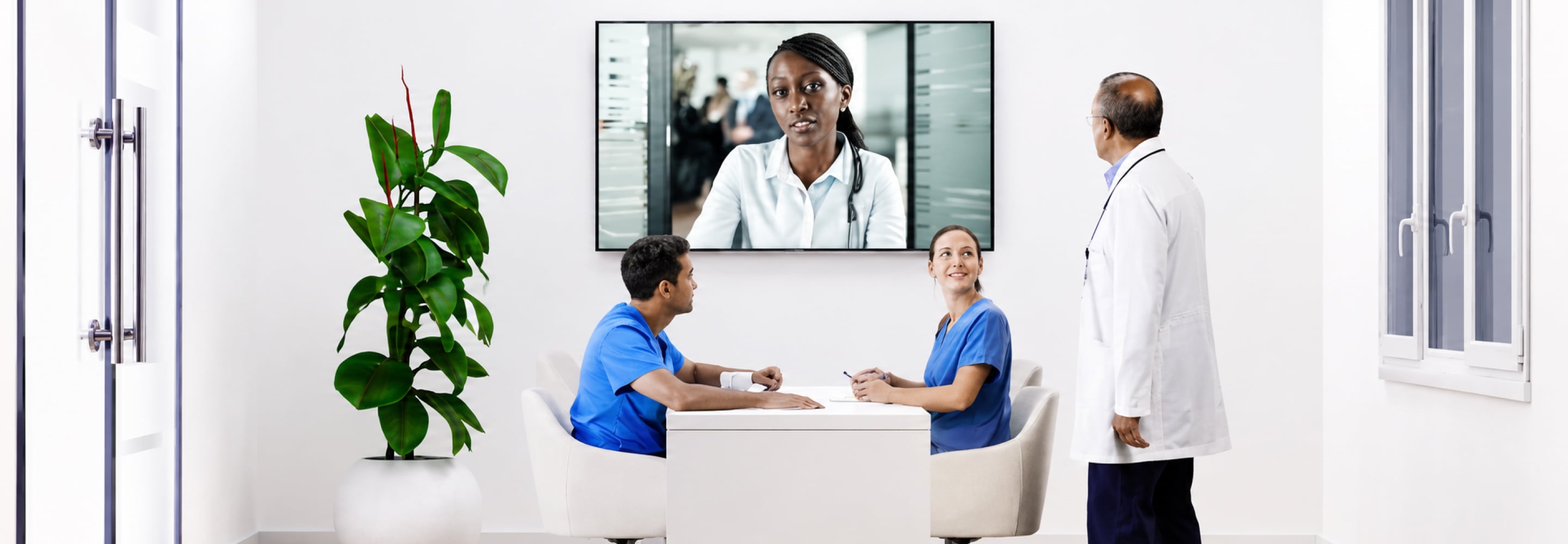 Patient and nurse in a clinic with a doctor on a video call on a wall-mounted screen