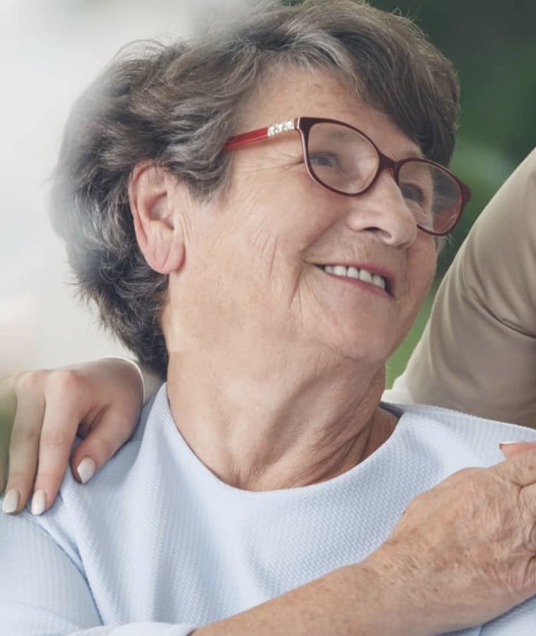 Smiling senior woman with a caregiver's hand on her shoulder