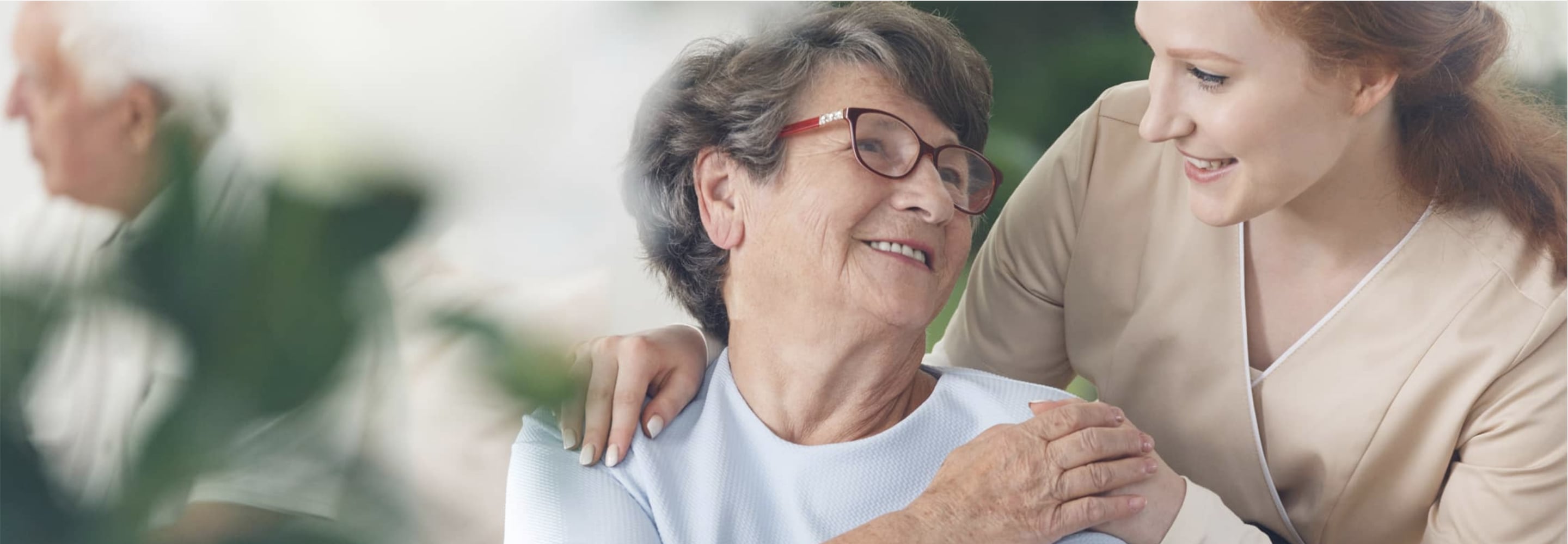 Smiling senior woman with a caregiver's hand on her shoulder