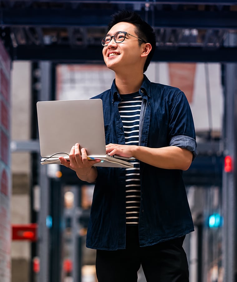 Smiling young man holding a laptop in a warehouse