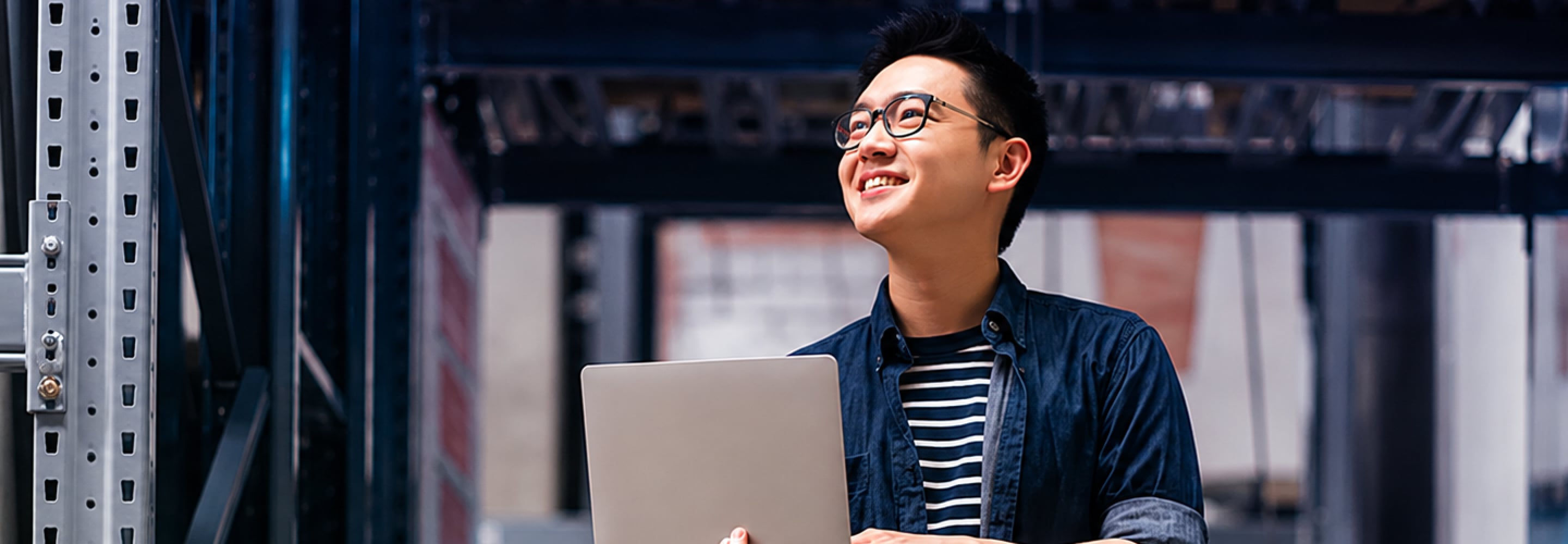 Smiling young man holding a laptop in a warehouse