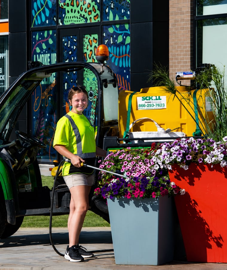 Landscaping crew member in a high-visibility shirt maintaining colorful flower beds