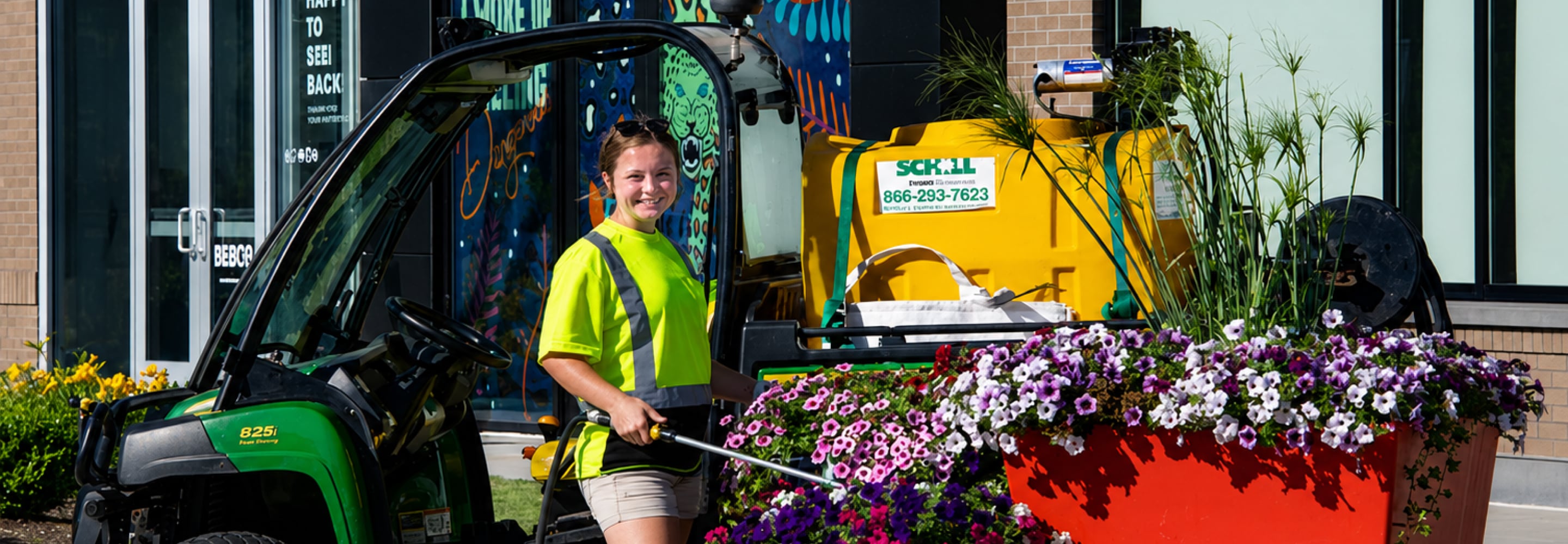 Landscaping crew member in a high-visibility shirt maintaining colorful flower beds