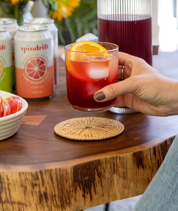 Spindrift sparkling water cans next to a glass of iced fruit drink with an orange slice