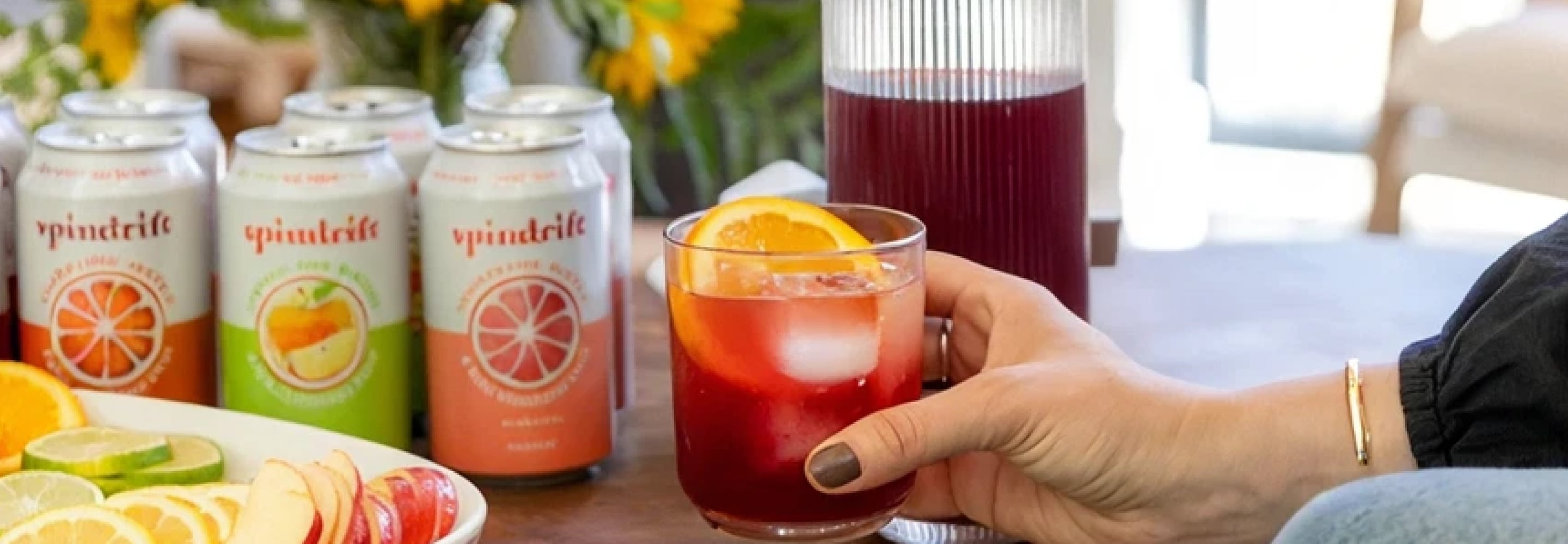 Spindrift sparkling water cans next to a glass of iced fruit drink with an orange slice