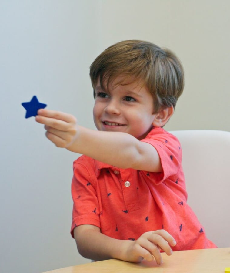 Smiling young boy holding up a blue star during a therapy session