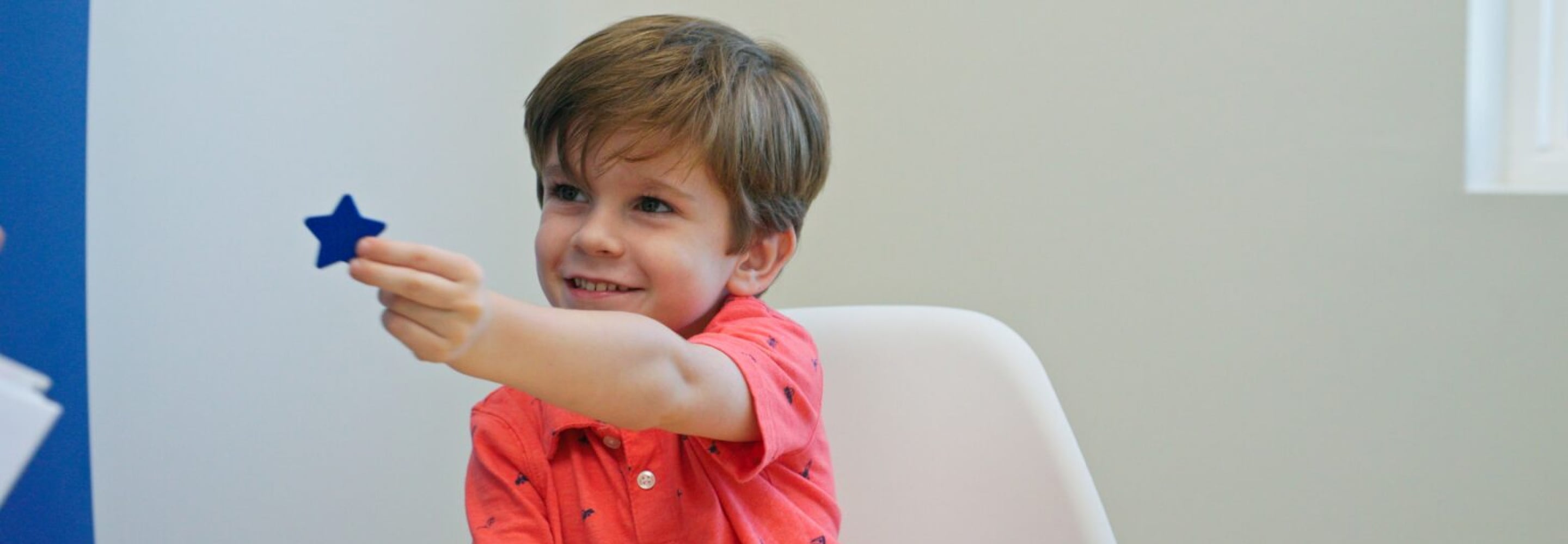 Smiling young boy holding up a blue star during a therapy session